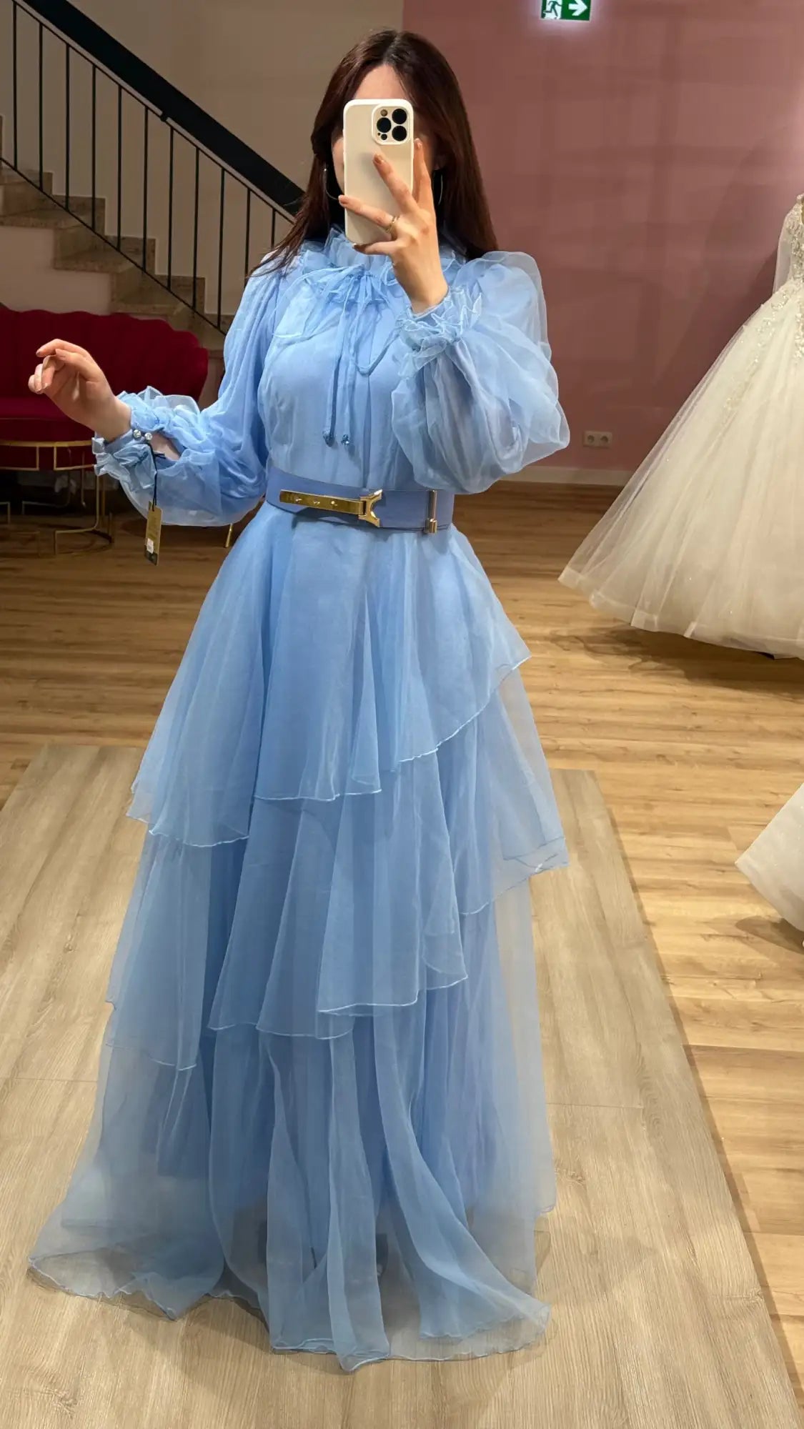 Ein fließendes hellblaues gestuftes Tüllkleid mit Puffärmeln und einem goldfarbenen Gürtel.