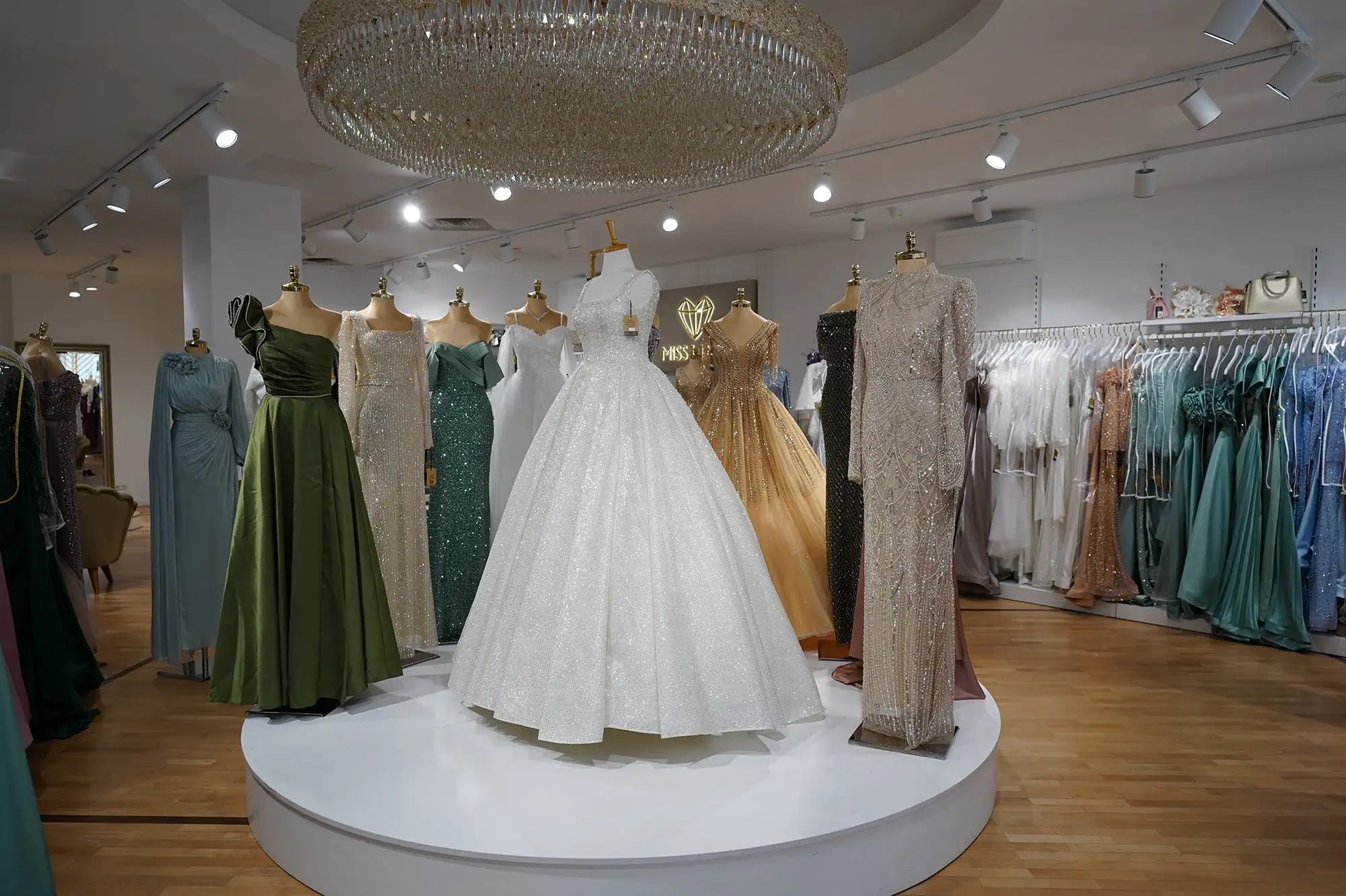 Ein weißes, voluminöses Ballkleid mit aufwendiger Spitzenverzierung und einem taillierten Oberteil wird auf einem zentralen Podest präsentiert.